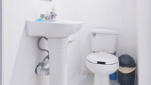 A small, white bathroom with a pedestal sink, a toilet, and a trash bin. - Mini apartment, centrally located, safe and comfortable (Villahermosa)