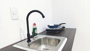 A kitchen with a stainless steel sink, a black faucet, a bottle of dish soap, and a frying pan on a portable stove. - Mini apartment, centrally located, safe and comfortable (Villahermosa)