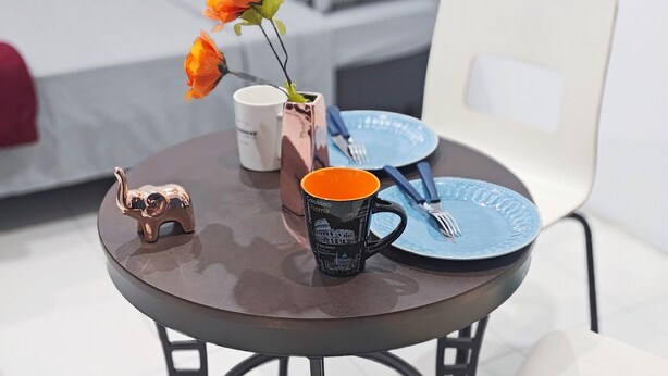 A round table with a coffee mug, a small elephant figurine, and a vase with orange flowers. There is a blue plate and a fork on the table. - Mini apartment, centrally located, safe and comfortable (Villahermosa)