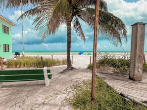 Ein Strand mit einer Holzstege, einem grünen Gebäude und einer Palme.