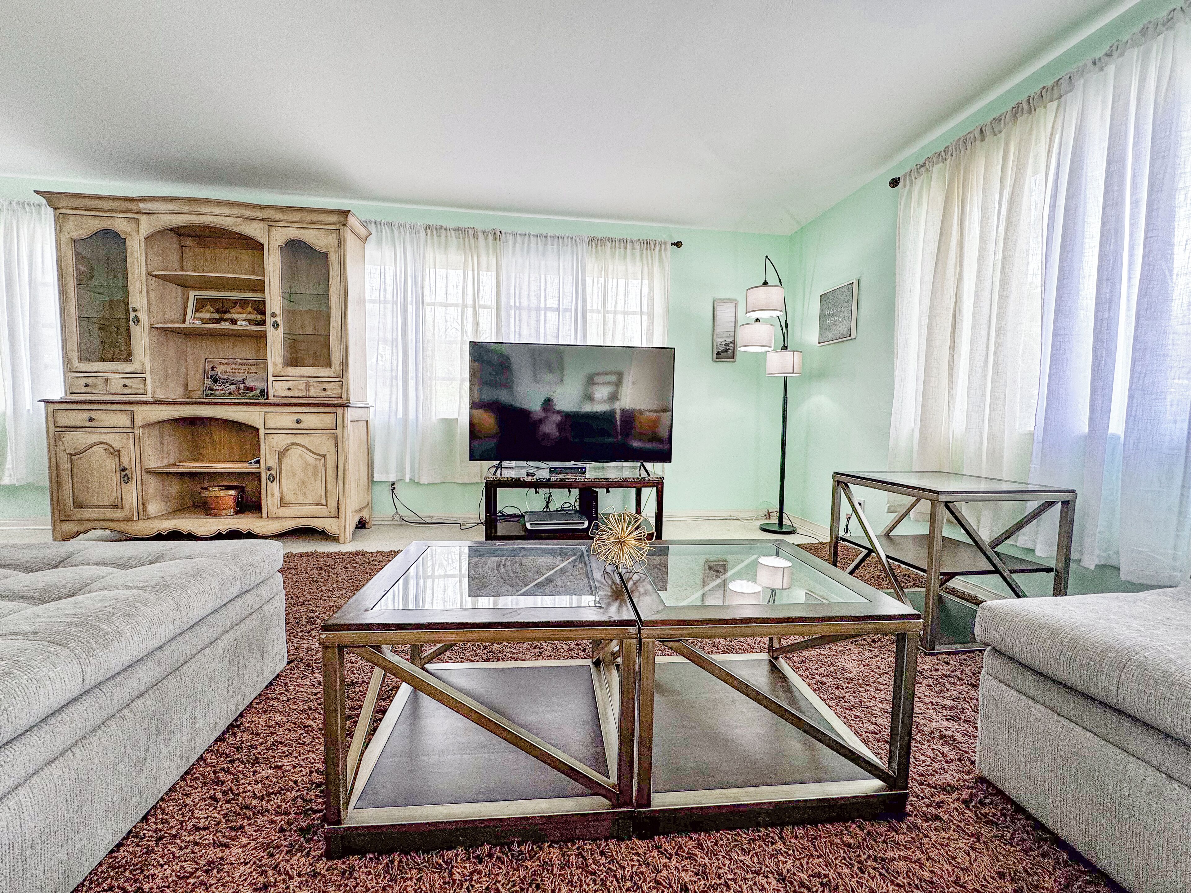 Una sala de estar con televisor, una mesa de centro de vidrio y un aparador.