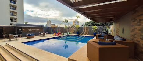 Una piscina al aire libre, sombrillas, sillones reclinables de piscina