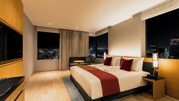 A modern hotel room with a large bed, a city view, a small table, and a TV.