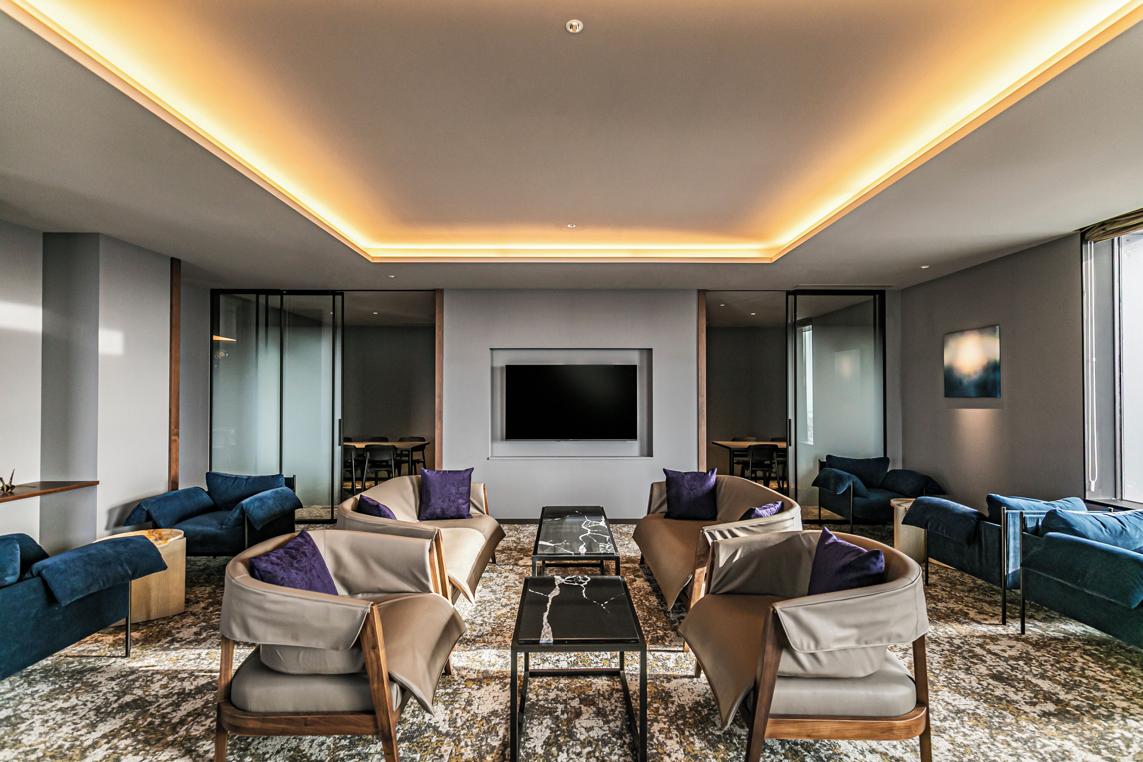A modern living room with a large flat-screen TV, comfortable seating, and a patterned carpet.