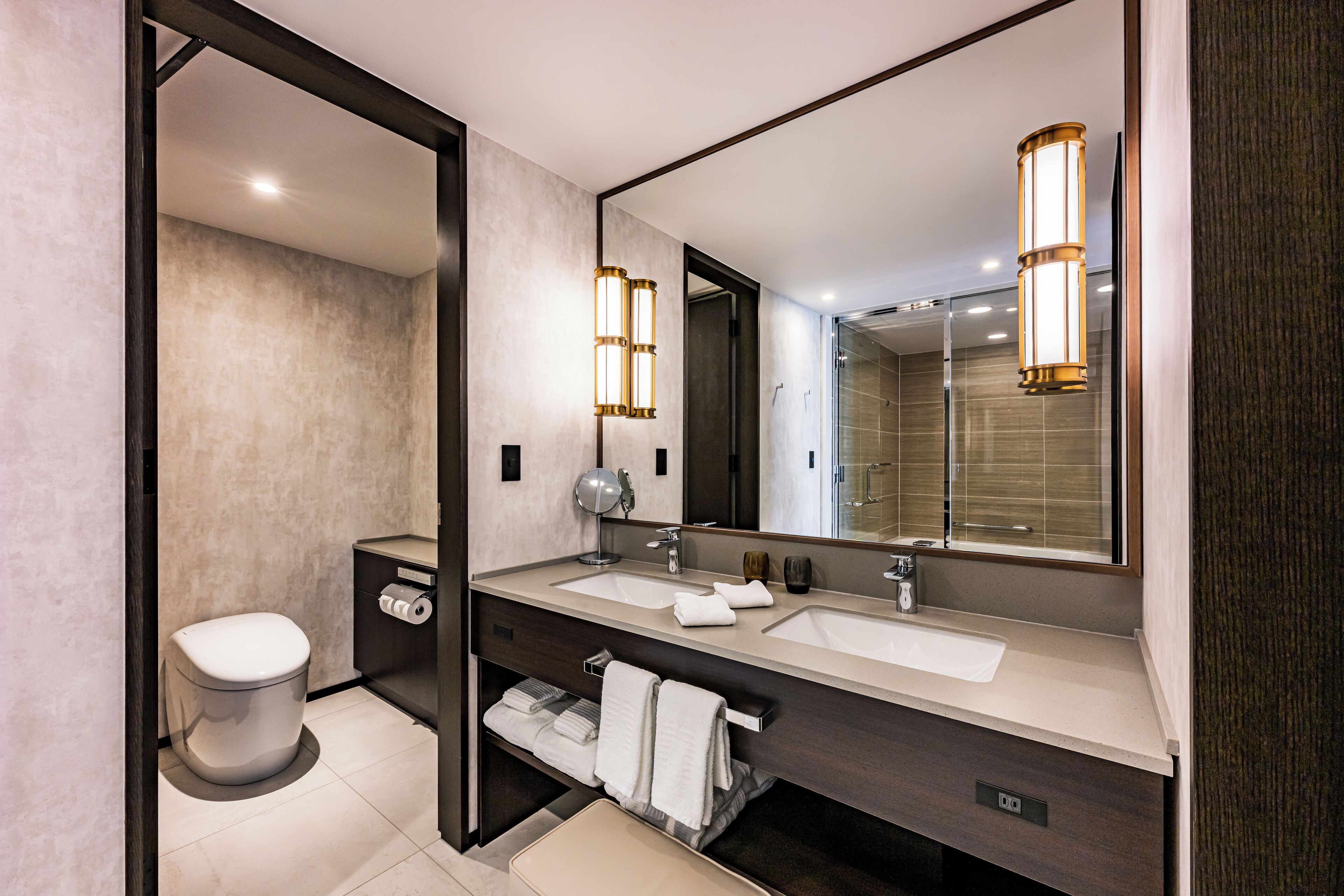 A modern bathroom with a large mirror, two sinks, and a toilet.