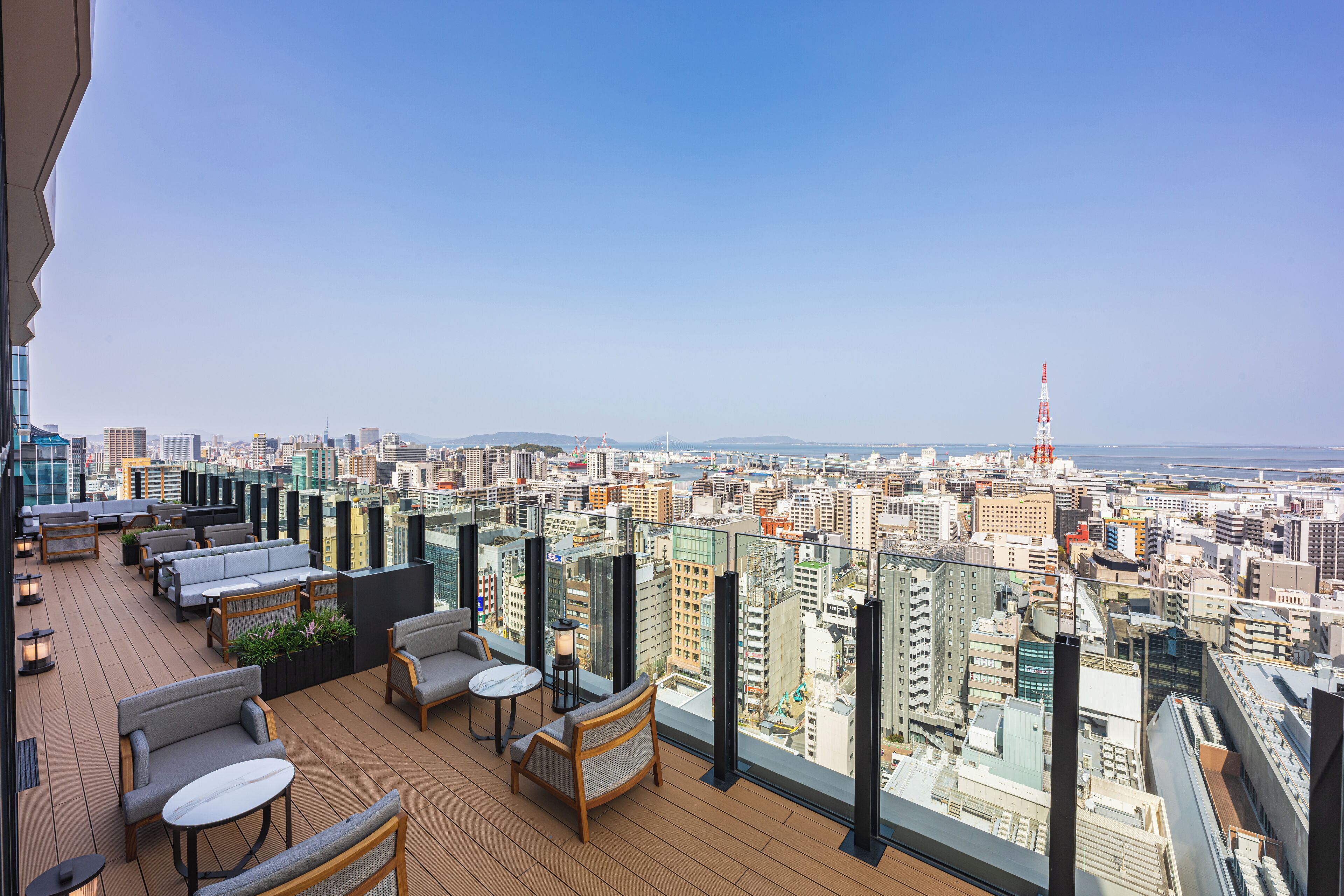 A high-rise building with a rooftop terrace featuring outdoor seating and a panoramic city view.