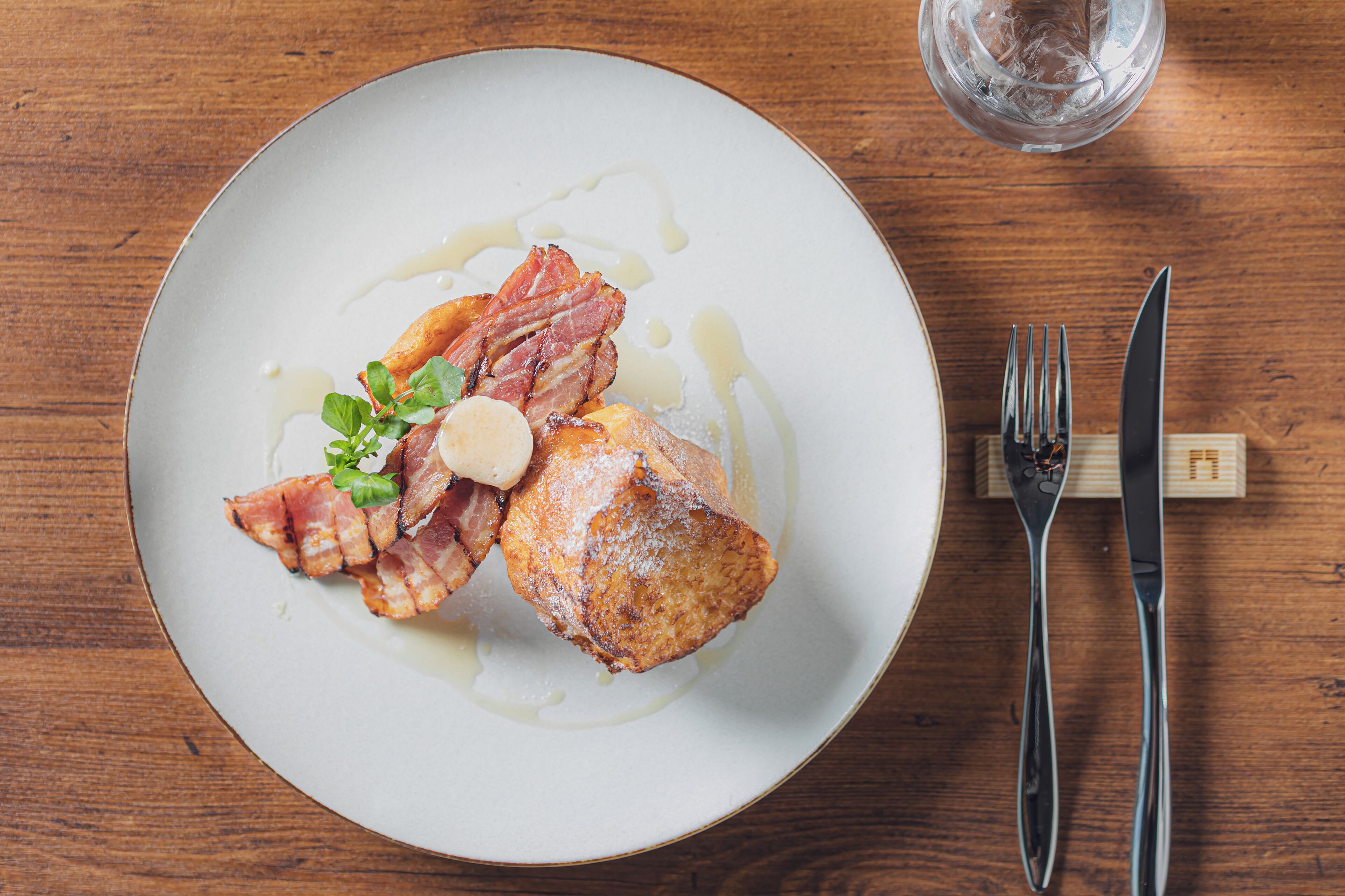 A plate of food with bacon and a pastry on a wooden table.