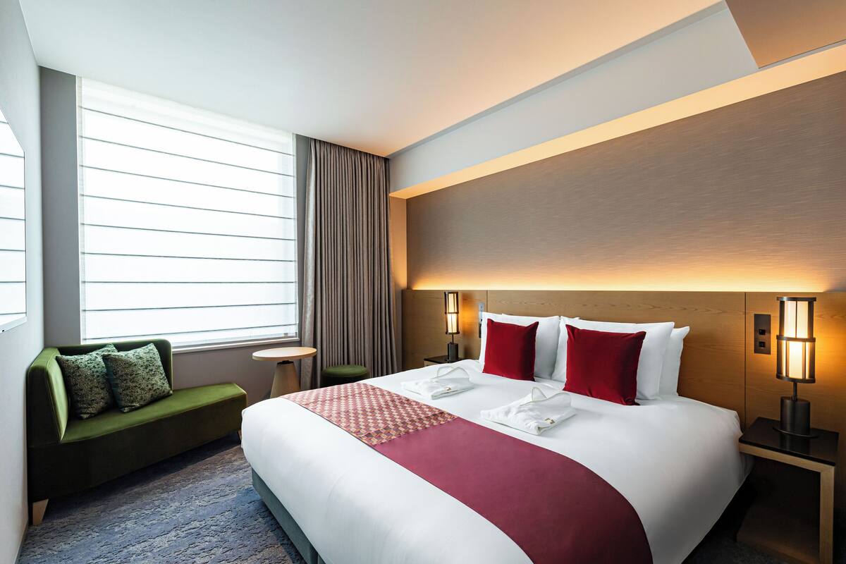 Quarto de hotel com uma cama grande, um sofá verde, uma mesa pequena e um abajur.