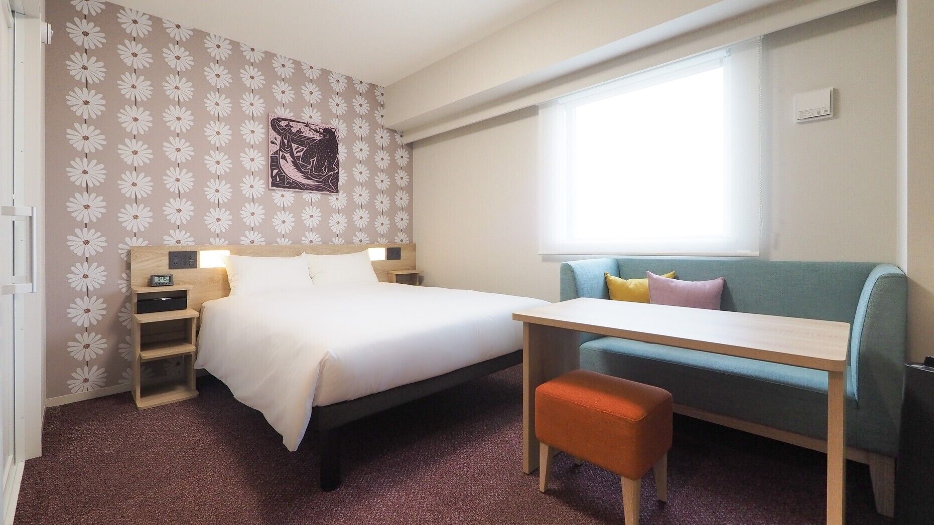 Una habitación de hotel con cama, escritorio, silla, sofá, un reloj de pared y una ventana.