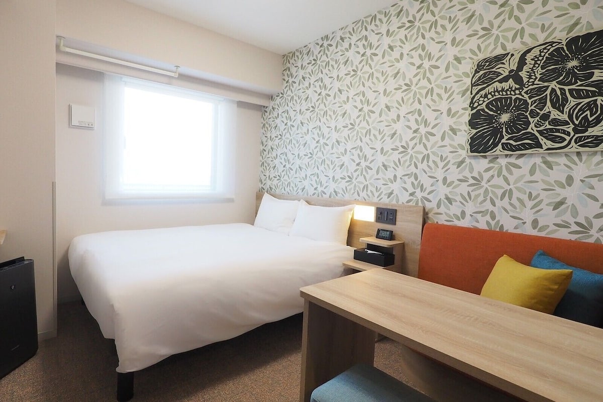Quarto de hotel com cama, mesa de cabeceira e janela.