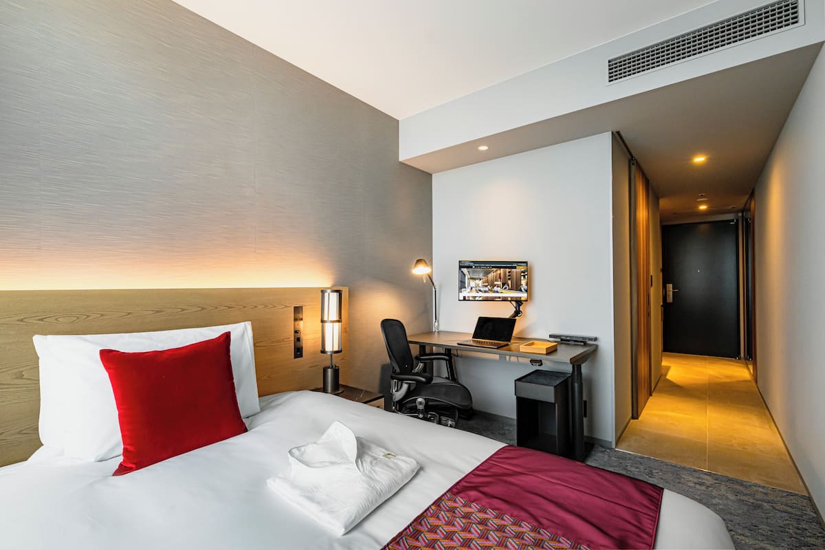 Quarto de hotel com cama, escrivaninha, cadeira e computador.