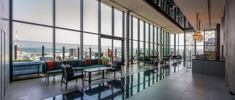 Un espacio interior amplio con ventanas grandes, una zona de estar con sofás y sillones, y un techo alto con vigas a la vista.