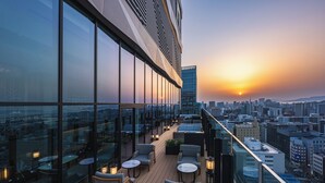 A rooftop terrace with glass walls, outdoor seating, and a cityscape view during sunset. - THE GATE HOTEL FUKUOKA by HULIC (Fukuoka)