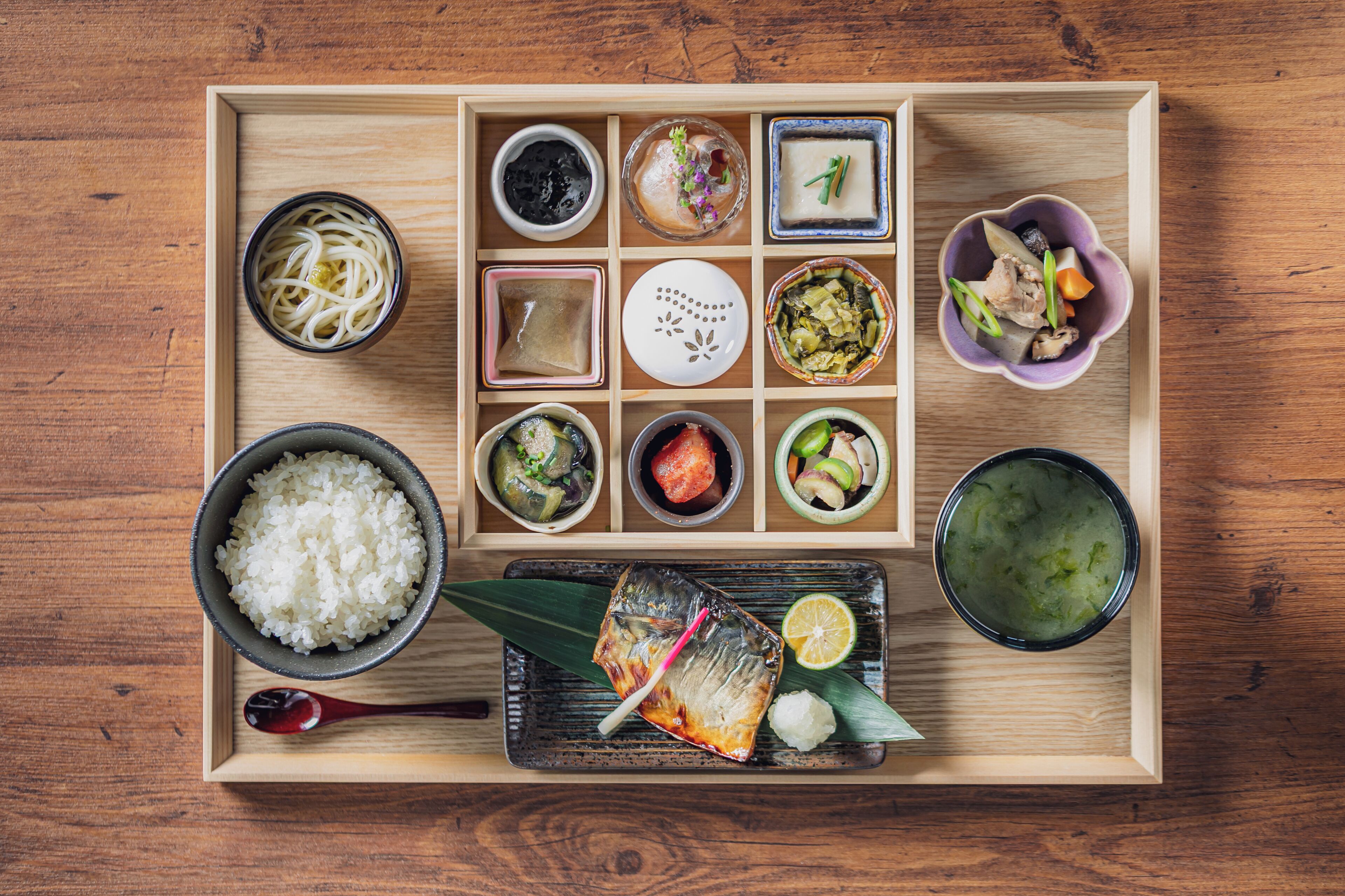 A wooden tray with various Japanese dishes including rice, fish, and pickled vegetables.