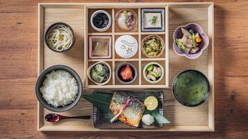 A wooden tray with various Japanese dishes including rice, fish, and pickled vegetables.