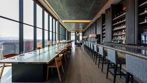 A modern bar with a long counter, multiple seating areas, and a view of the city through large windows. - THE GATE HOTEL FUKUOKA by HULIC (Fukuoka)