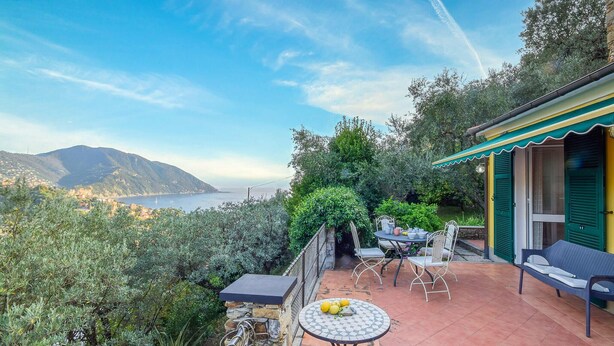 Une terrasse avec une table et des chaises, un mur en pierre et une vue sur la mer et les montagnes.