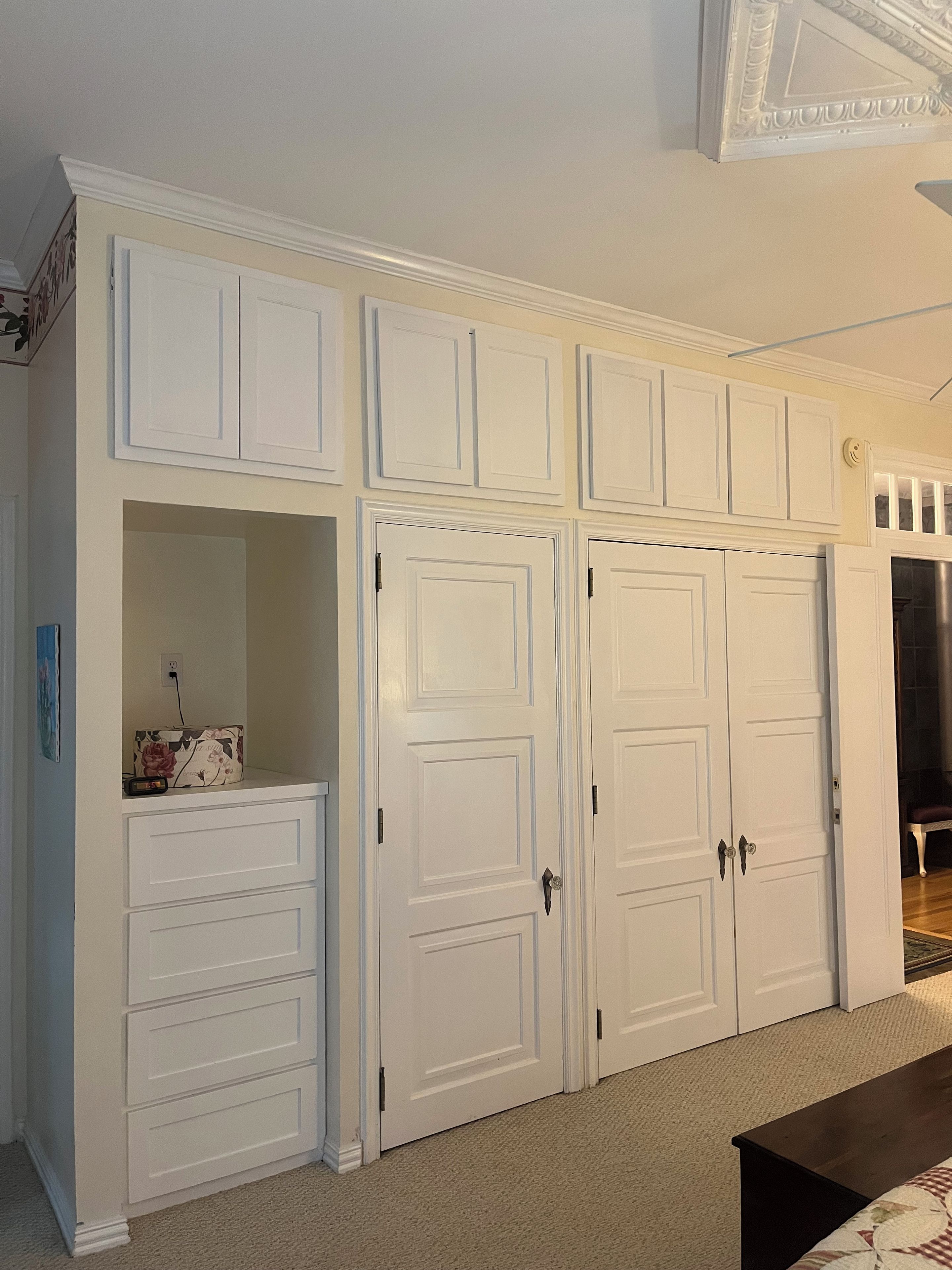 Une pièce avec une armoire blanche, une petite étagère sur laquelle se trouve une horloge, et un banc.