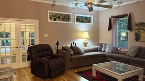 A living room with a sectional sofa, a recliner, a glass-top coffee table, and a ceiling fan.
