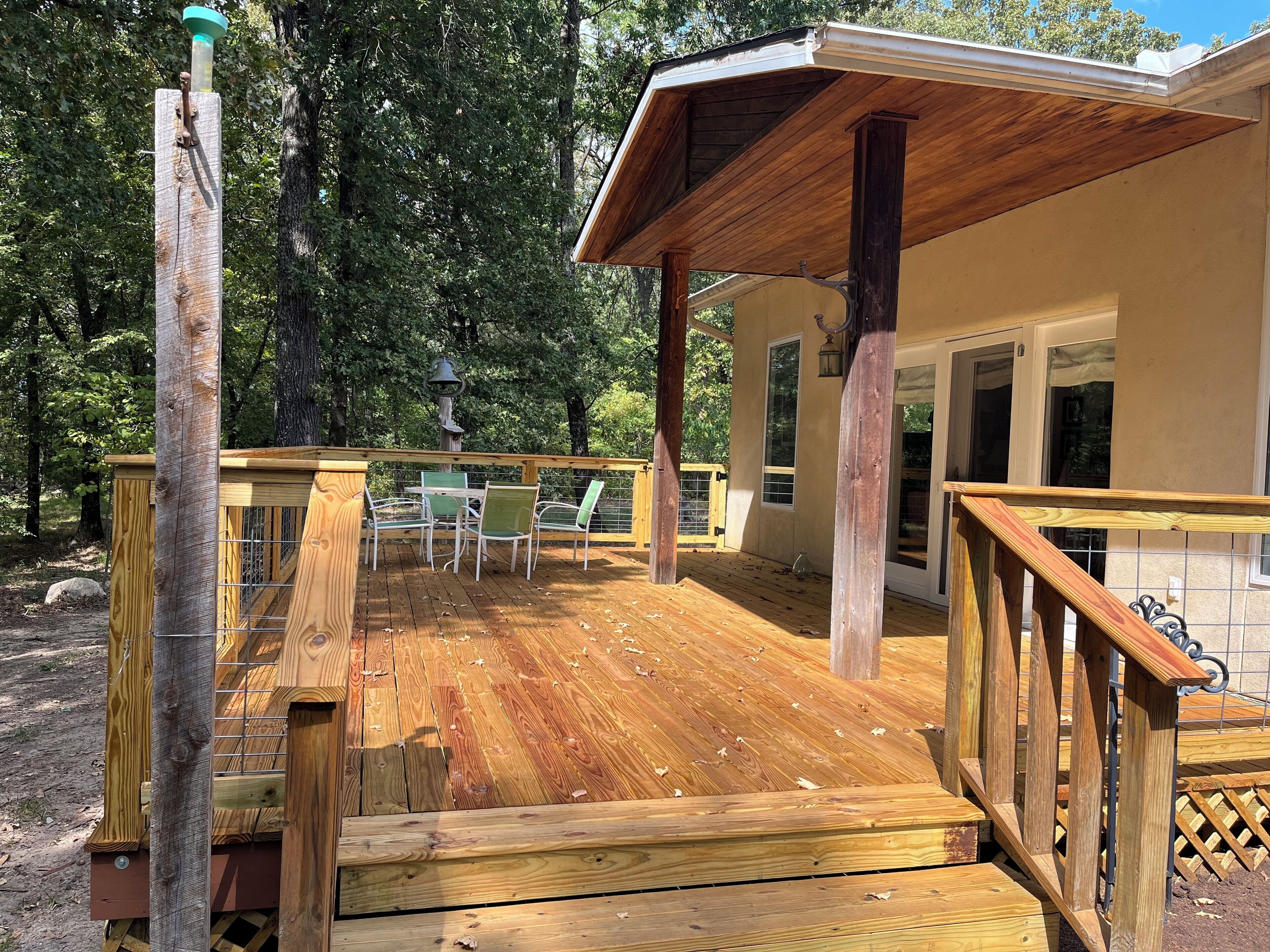 Una terraza de madera con una mesa y sillas, un pérgola y vistas a una casa con puerta corredera de vidrio.