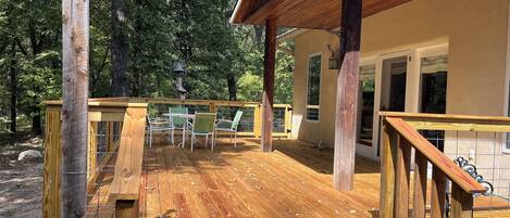 A wooden deck with a table and chairs, a pergola, and a view of a house with a sliding glass door.