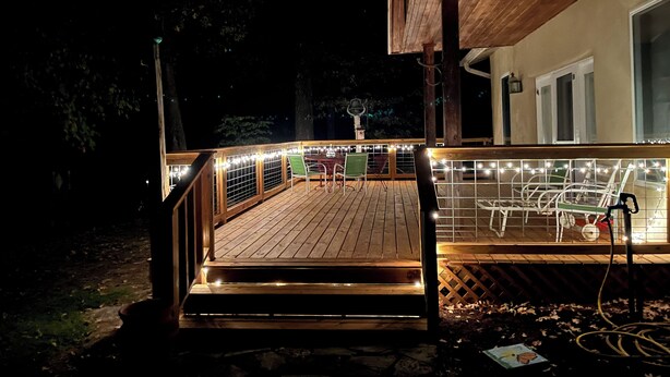 A wooden deck with string lights, outdoor furniture, and a view of a house.