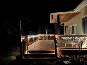 Eine Holzterrasse mit Lichterketten, Gartenmöbeln und Blick auf ein Haus.