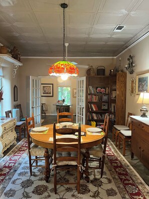 Un comedor con una mesa redonda de madera, sillas, un tapete estampado y una lámpara colgante de vitral.