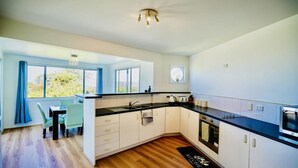 Una cocina moderna con encimera negra, armarios blancos y ventana con vistas a la vegetación.