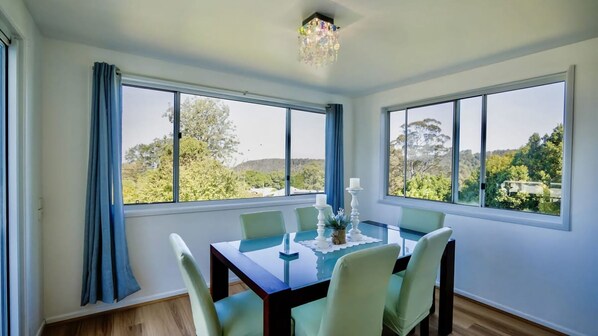 A dining room with a table set for six, large windows with a view of trees and hills, and a chandelier.