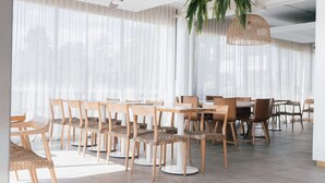 A modern dining area with round tables and chairs, large windows with sheer curtains, and a hanging woven light fixture. - Kiama Coast | Beach, Balcony & Barbecue (Kiama)