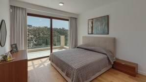 A bedroom with a large bed, a view of a hillside, and a painting on the wall.