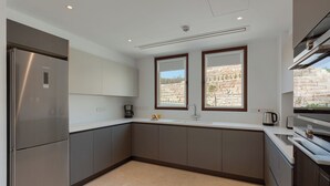 A modern kitchen with a stainless steel refrigerator, a built-in oven, a sink with a faucet, and two windows providing views of the outdoors.
