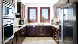A modern kitchen with stainless steel appliances, wooden cabinets, a double sink, and a view through two windows. - Spectacular Sea Views Await, Paphos Villa 1481 (Paphos)