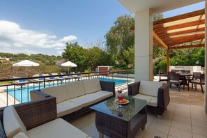A poolside area with wicker furniture, a glass table, and umbrellas. - Experience Unmatched Luxury in a Serene Oasis (Paphos)