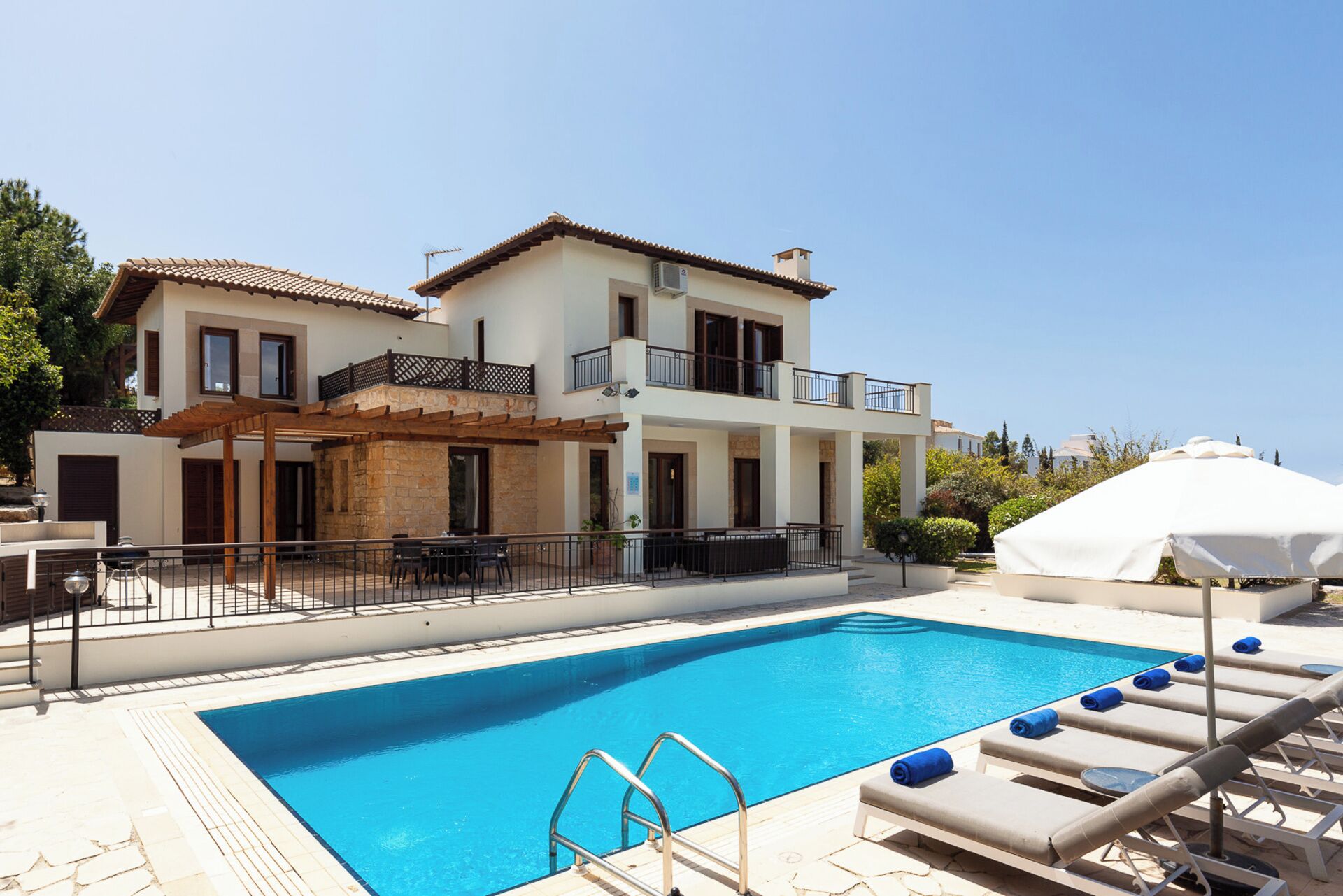 A two-story house with a swimming pool, outdoor furniture, and a covered area.