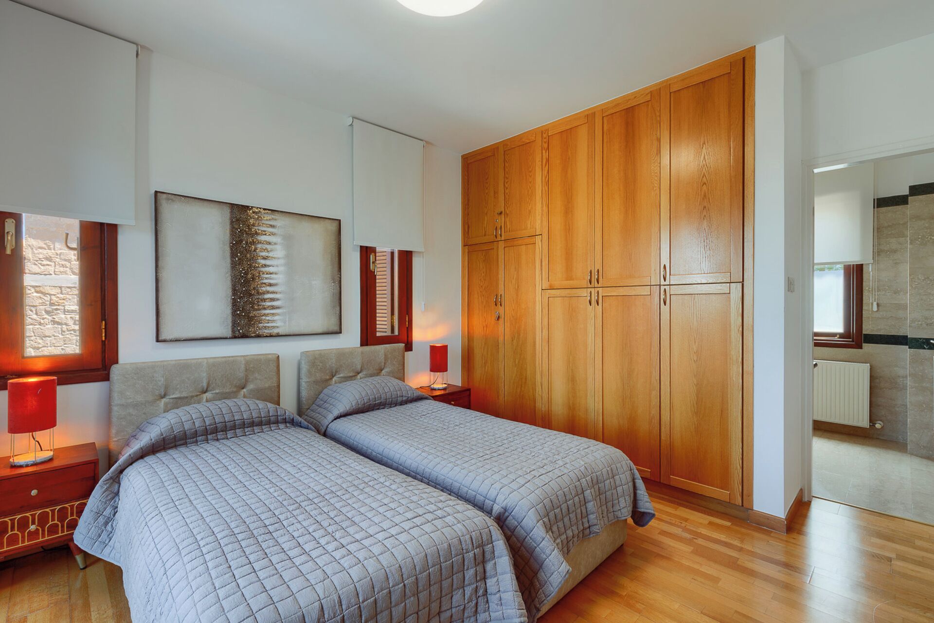 Een slaapkamer met twee bedden, een houten garderobe en een schilderij aan de muur.