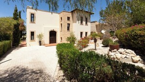 A two-story building with a stone facade, a paved driveway, and various plants and shrubs in the foreground.