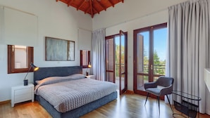 A bedroom with a large bed, a nightstand, a desk, a chair, and a balcony with curtains.