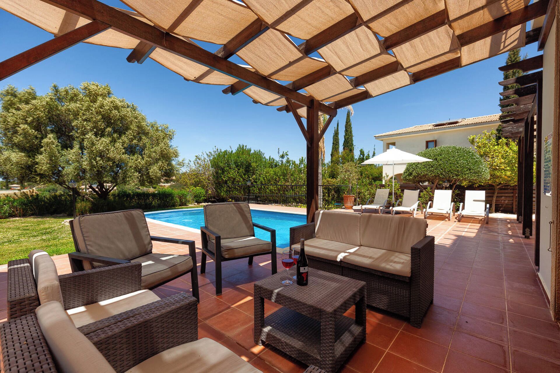 An outdoor patio with wicker furniture, a pool, and a pergola providing shade.