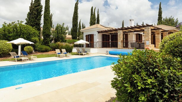 Une piscine entourée de verdure et de grands arbres, avec des chaises longues et des parasols.