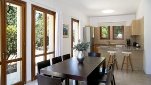 A dining area with a wooden table and chairs, a vase with plants, and a kitchen with stools and cabinets. - Unwind in Luxury: Your Perfect Family Escape (Paphos)