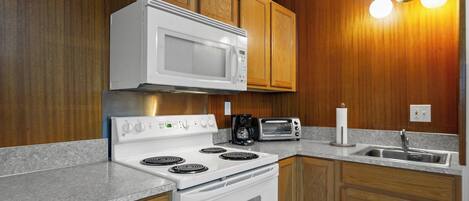 A kitchen with wooden cabinets, a white microwave, a stove, a toaster, and a sink.