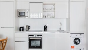 Una cocina moderna con armarios blancos, microondas, cafetera, lavavajillas y lavadora.
