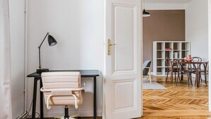 Een kamer met een witte deur, een bureau met stoel, een lamp, en een zithoek met stoelen en een tafel.