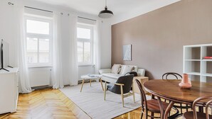 Een moderne woonkamer met een bank, salontafel en een eettafel. Er is een radiator, een wit kastje en een raam met gordijnen.