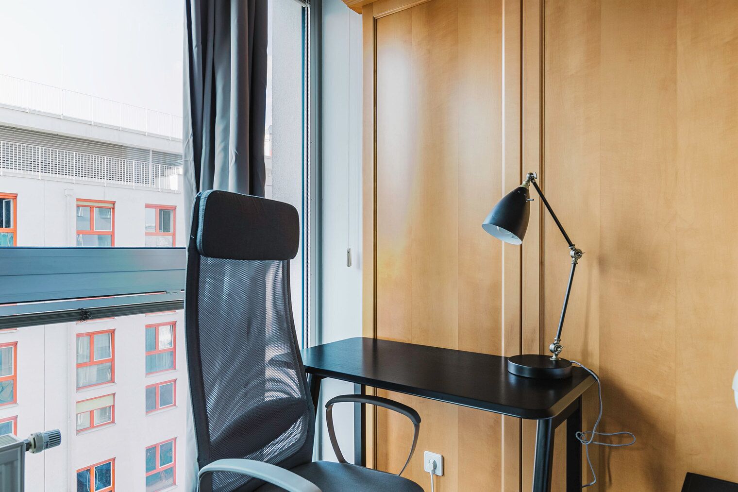 A hotel room with a desk, chair, and lamp.