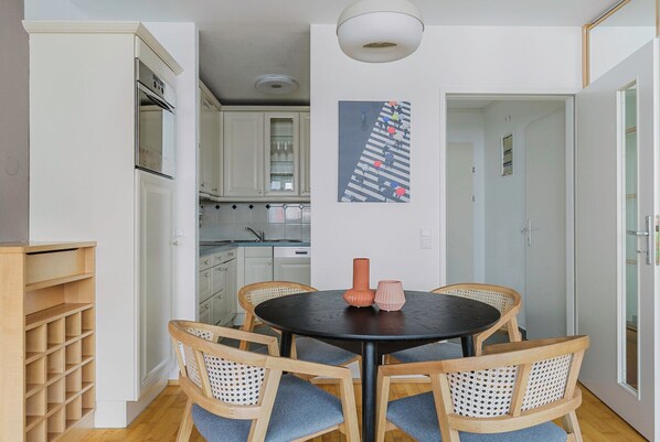 Une cuisine moderne avec des meubles blancs, une table à manger et quatre chaises, ainsi qu’un luminaire suspendu au plafond.