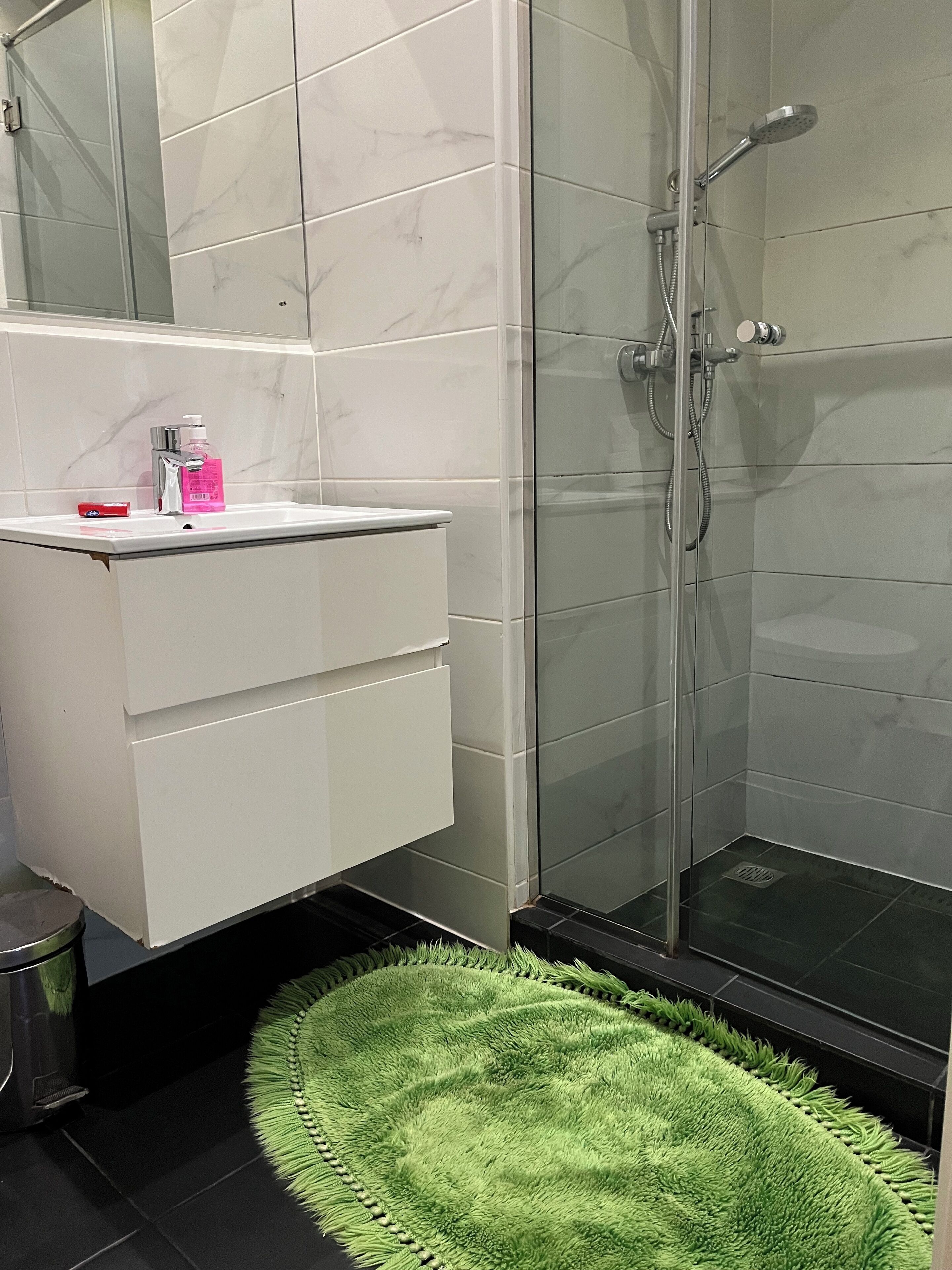 A bathroom with a white vanity, a glass shower enclosure, and a green rug on the floor.