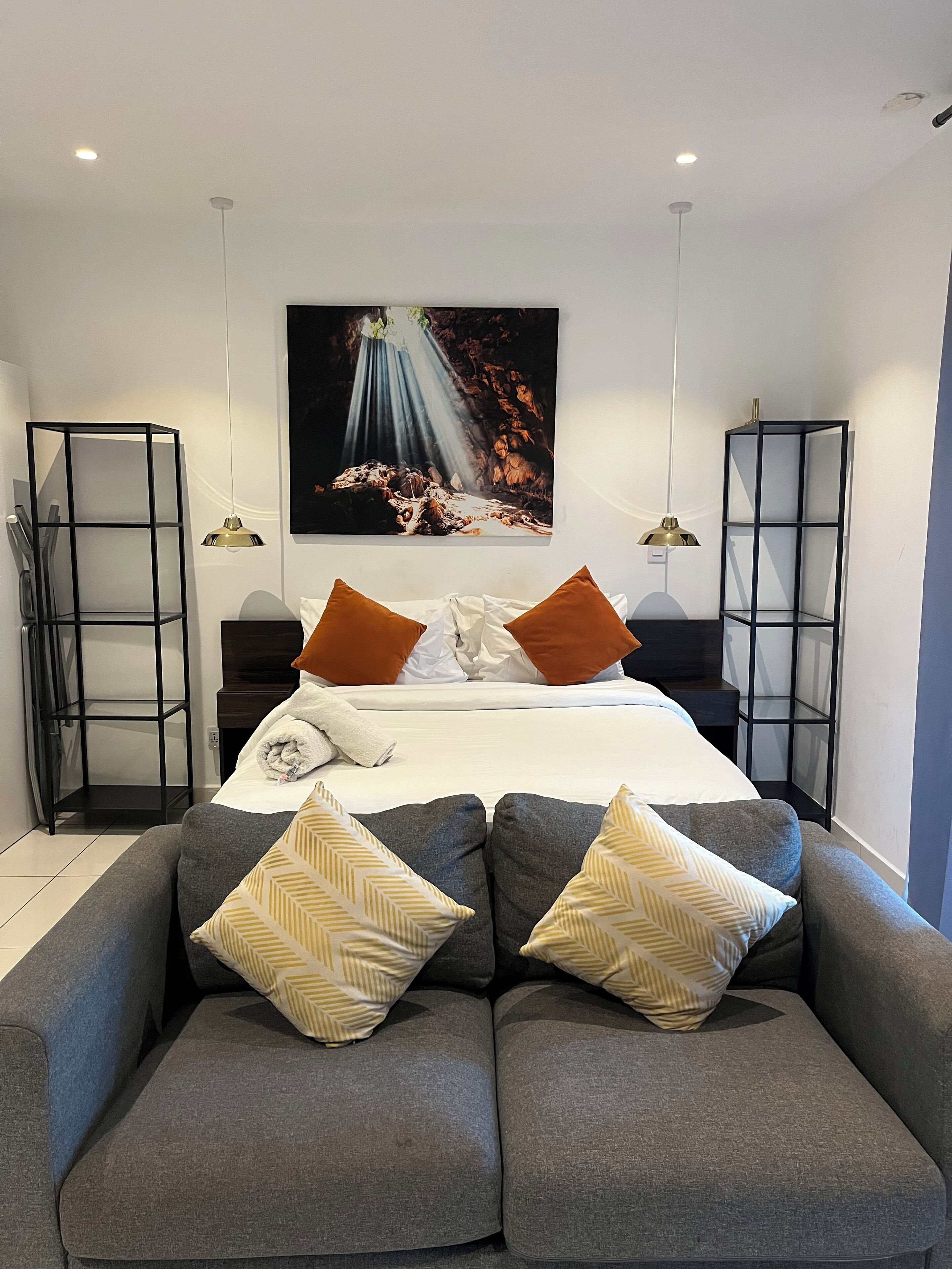 A modern hotel room with a large bed, a sofa, two side tables, and a large painting on the wall.